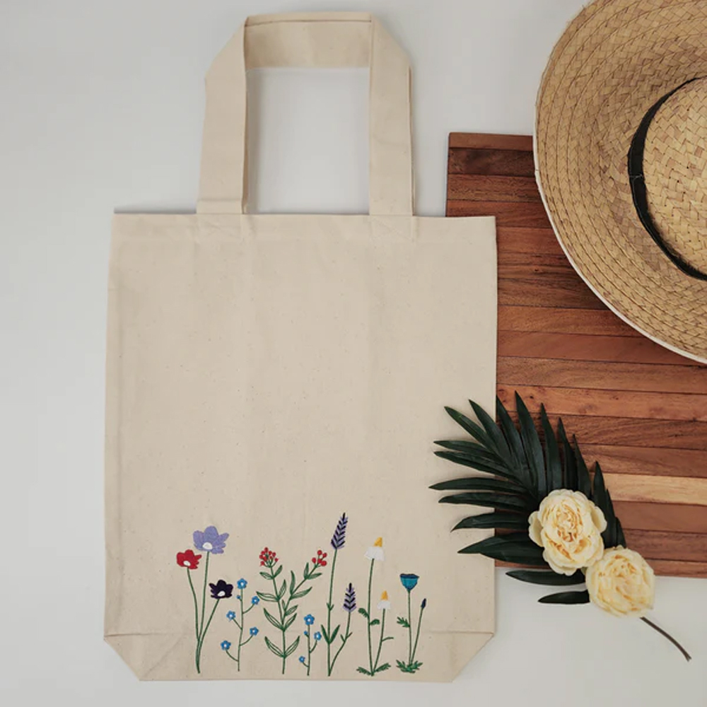 Natural ecru cotton canvas tote bag with a multicolour embroidered wildflower design across the lower front